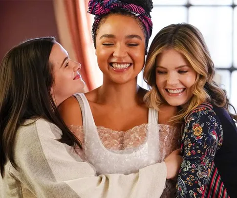 Three women smiling and embracing in a warm hug, highlighting friendship and joy.