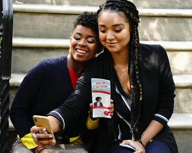 Two people taking a selfie on steps, holding a flyer that says "Vote for Kat Edison."