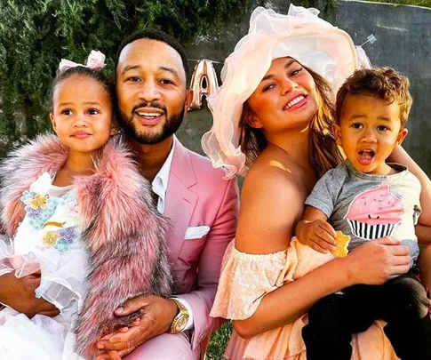 A family picture featuring a man in a pink suit and a woman in a sun hat with two children, smiling outdoors.