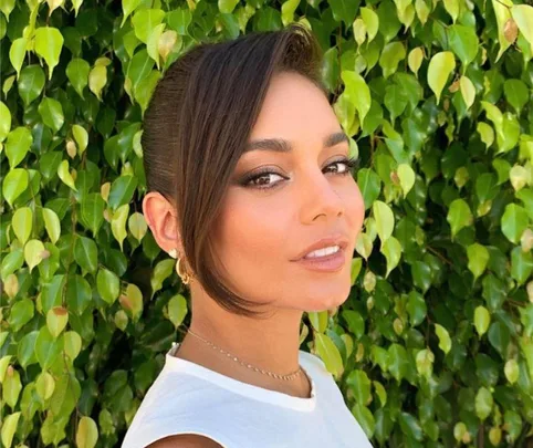 Person with a side fringe hairstyle poses outdoors against a leafy background.