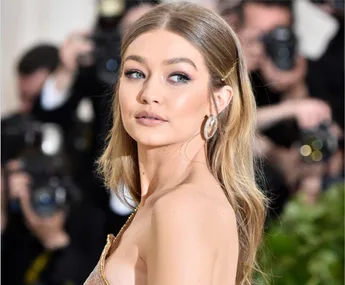 Person in an elegant dress poses on a red carpet, surrounded by photographers.