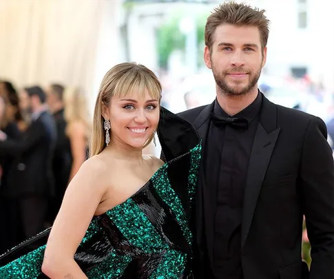 A couple posing at a formal event, with the woman in a sparkling green dress and the man in a black suit and bow tie.