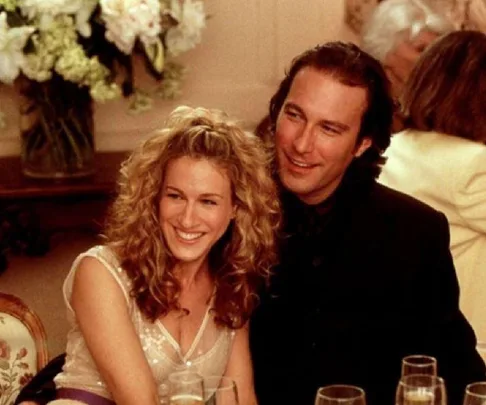 A couple, smiling at a party, sit closely together with glasses in front of them.