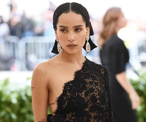 A woman in a black lace dress with earrings at a formal event, with blurred attendees in the background.