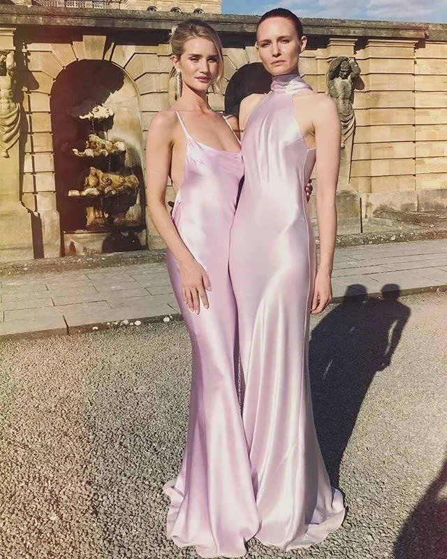 Two women in light pink satin gowns standing outside a historic building with arched fountains.