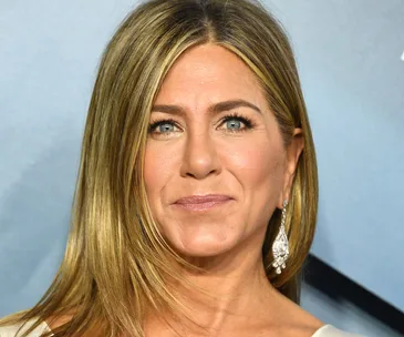 A person with long blonde hair and earrings smiles at a formal event.