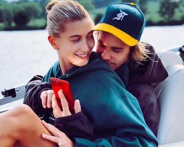 A couple embracing on a boat, with one holding a red phone and smiling, set against a lake background.