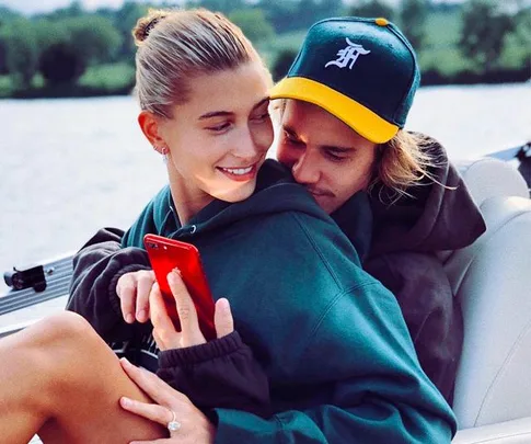 A couple embracing on a boat, with one holding a red phone and smiling, set against a lake background.