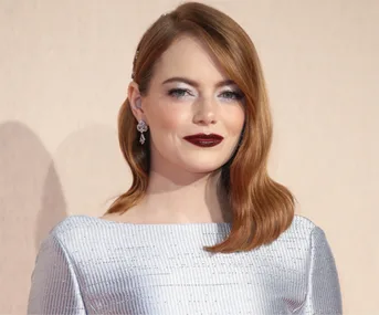 Woman with shoulder-length red hair, wearing silver dress and earrings, smiling at an event.