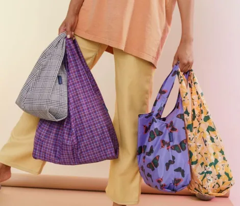 Person holding four reusable shopping bags with different patterns: plaid, grid, butterfly, and floral.