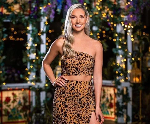 Woman in a leopard print dress poses outside with string lights in background.