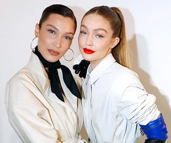 Two women pose together, one with hoop earrings and dark lipstick, the other with a sleek ponytail and bright red lipstick.