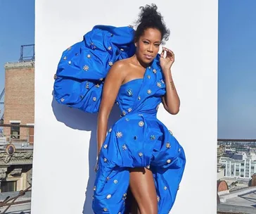 Person in a bold blue dress with floral details, posing against a white backdrop on a rooftop.