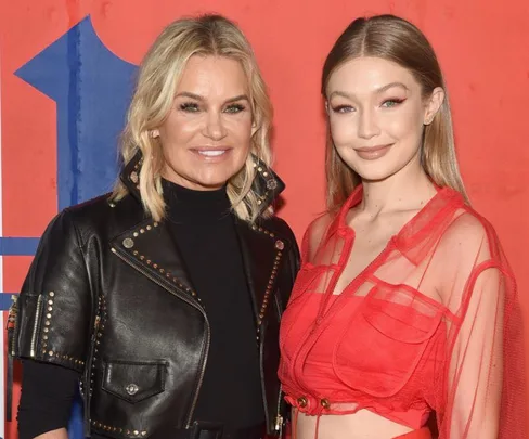 Two women smiling at a stylish event; one in a black jacket, the other in a red outfit, posing against a colorful backdrop.