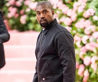 Man in a dark jacket looking back, standing in front of a backdrop of pink flowers and steps.