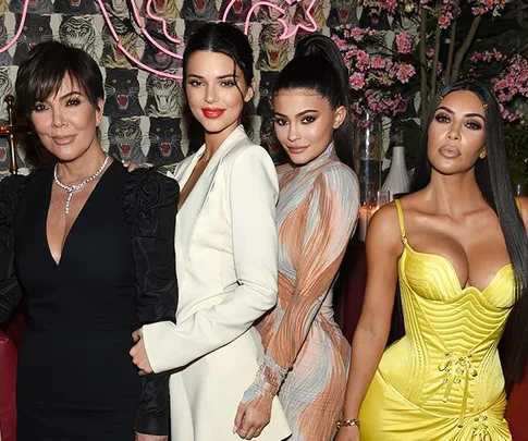 Kris Jenner standing with Kendall, Kylie, and Kim, dressed glamorously at an event with a vibrant floral backdrop.