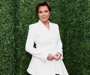 Woman in a white suit poses in front of green foliage.