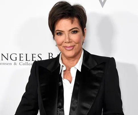 A person in a black suit with a white shirt smiling at a formal event backdrop.