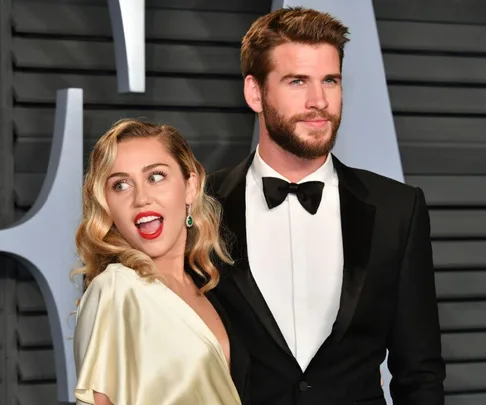 A couple poses on the red carpet, dressed in formal attire, at a glamorous event backdrop.