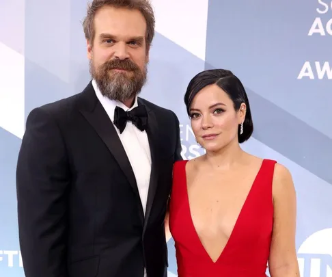 A couple dressed formally at an awards event, man in a tuxedo, woman in a red dress, posing for a photo.