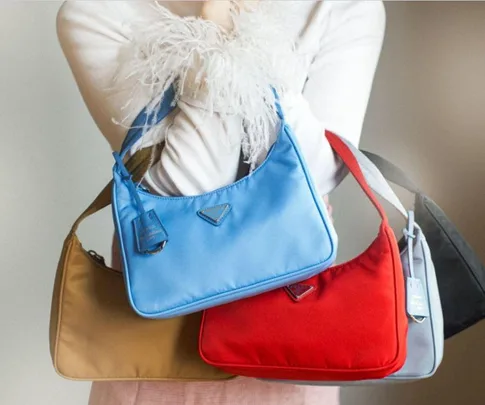 A person holds four colorful handbags: blue, red, light blue, and brown.