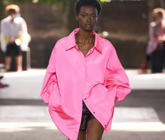 Model walking runway in oversized pink shirt and black shorts at Milan Fashion Week 2020.