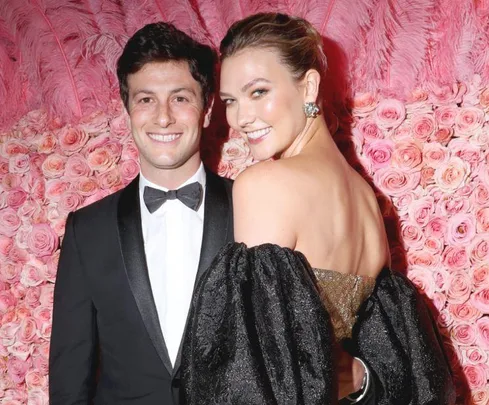 A smiling couple poses in formal attire against a backdrop of pink roses.