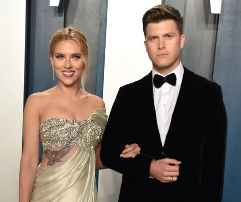 A couple poses together at an event, the woman wearing a bejeweled gown and the man in a black tuxedo.