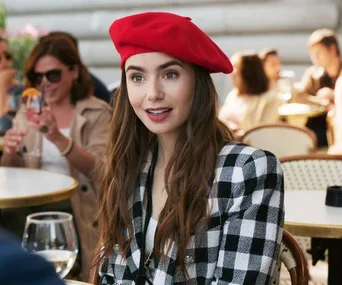 Woman in a red beret and checkered jacket sitting at an outdoor café table, smiling.