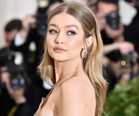 A woman with long blonde hair poses elegantly at a formal event, with photographers in the background.