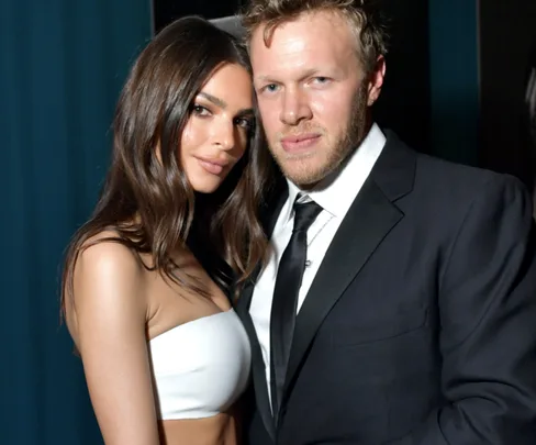 A woman in a white outfit poses closely with a man in a suit, both looking towards the camera.