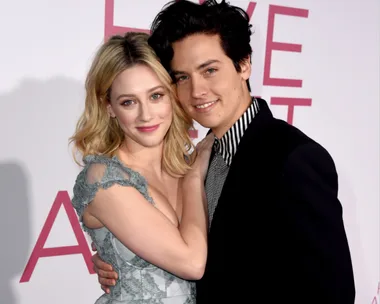 A couple smiling and embracing at a red carpet event.