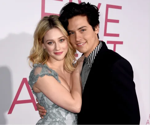 A couple smiling and embracing at a red carpet event.