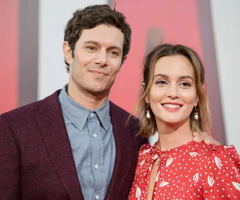 A man in a maroon suit and a woman in a red dress with heart patterns smiling together at an event.