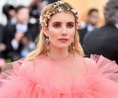 A woman in a pink tulle dress with floral hair accessories at a formal event, looking forward.