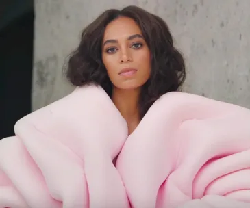 Person in a voluminous pink outfit poses against a gray textured background.