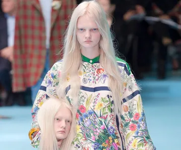 Model in floral outfit holds realistic replica of her head on runway.