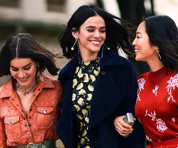 Three women walking, smiling and chatting, dressed in colorful and stylish outfits.