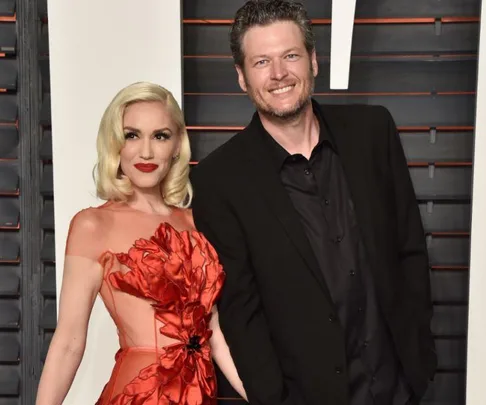 A couple smiling in formal attire; she wears a red dress, he wears a black suit.