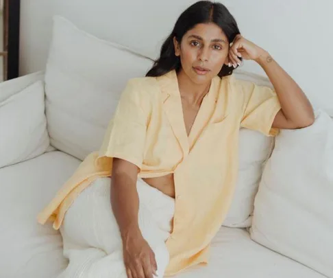 A woman lounging on a couch wearing a light yellow short-sleeve shirt and white pants, with a relaxed expression.