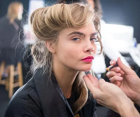 Model with styled hair and bright lipstick applies makeup backstage.