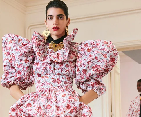 A model wearing a floral dress with puffed sleeves and bold jewelry at Paris Fashion Week Spring/Summer 2021.