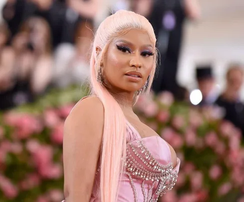 Pink-haired woman in an elegant dress at a formal event with flowers in the background.