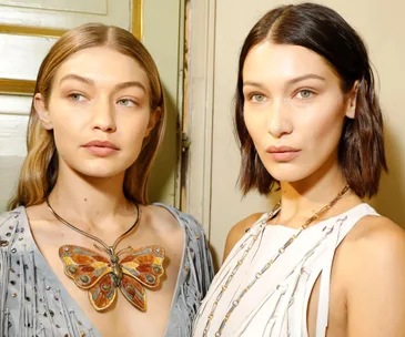 Two women posing together, wearing stylish necklaces and elegant outfits.