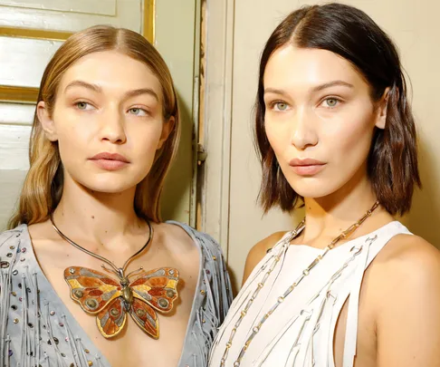 Two women posing together, wearing stylish necklaces and elegant outfits.