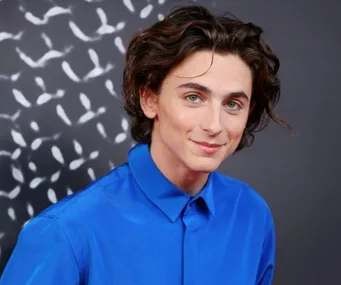 A person smiling and wearing a blue shirt in front of a patterned background.