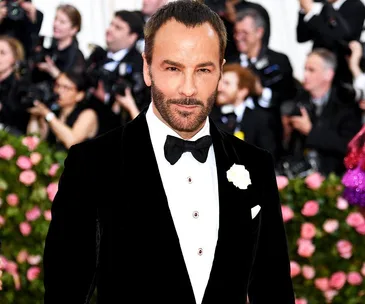 Man in a black tuxedo with a bow tie at a formal event, surrounded by photographers and pink floral decorations.