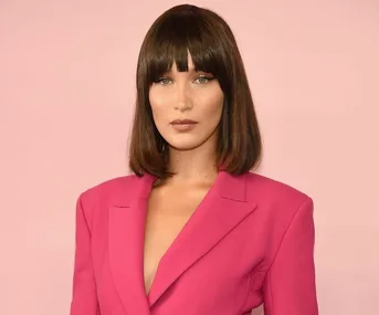 Fashion model wearing a bright pink blazer with a straight bob hairstyle against a soft pink background.