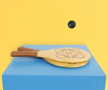 Two wooden paddles with logo and a black ball on a blue surface against a yellow background.