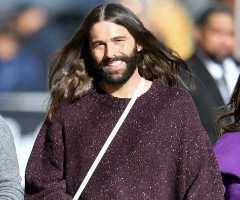 Person with long hair and a beard, wearing a purple sweater, smiling outdoors.